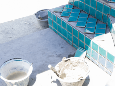 Professional pool tile installation with blue ceramic tiles Blue ceramic pool tiles being installed on pool steps with tools and mortar nearby
