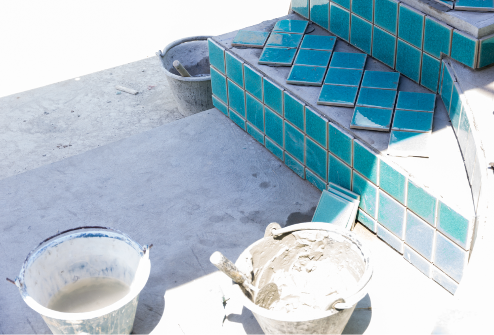 Blue ceramic pool tiles being installed on pool steps with tools and mortar nearby